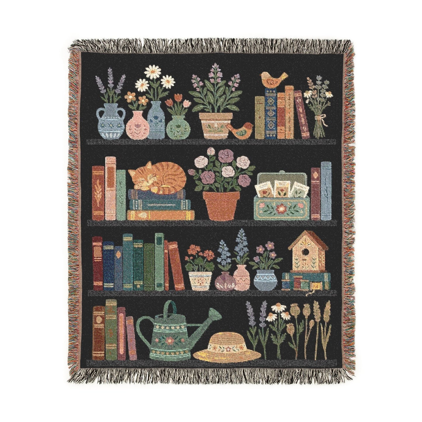 A rectangular woven throw blanket with fringe on all sides, featuring a black background and vertical panels of illustrated books, flowers, vases, a birdhouse, wheat, and a watering can.